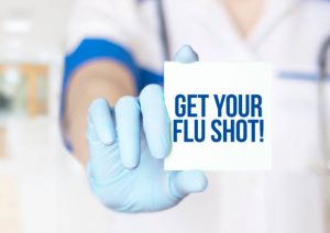 Doctor holding a card with the text "Get your flu shot" written on it, close-up of hand.                              