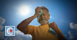 Man outdoors in sunlight, pressing a towel to the right side of his forehead while holding a second towel in his other hand.